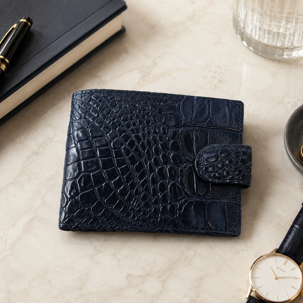 Deep navy Langham crocodile wallet displayed on a luxury marble table with refined accessories