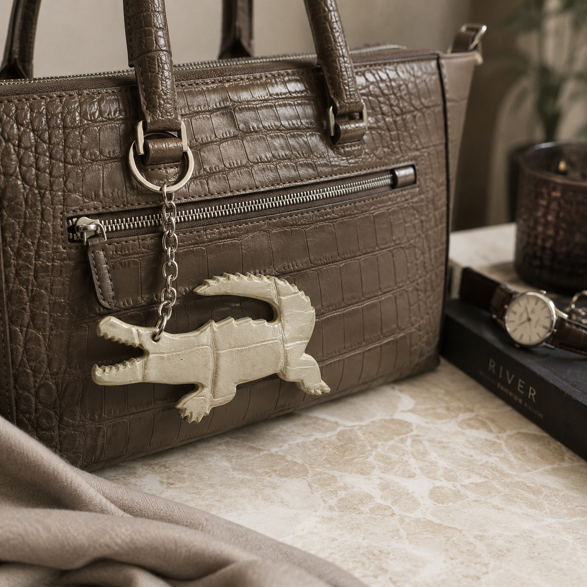 Ivory Pearl Siamese crocodile leather key charm hanging from a taupe crocodile-textured handbag
