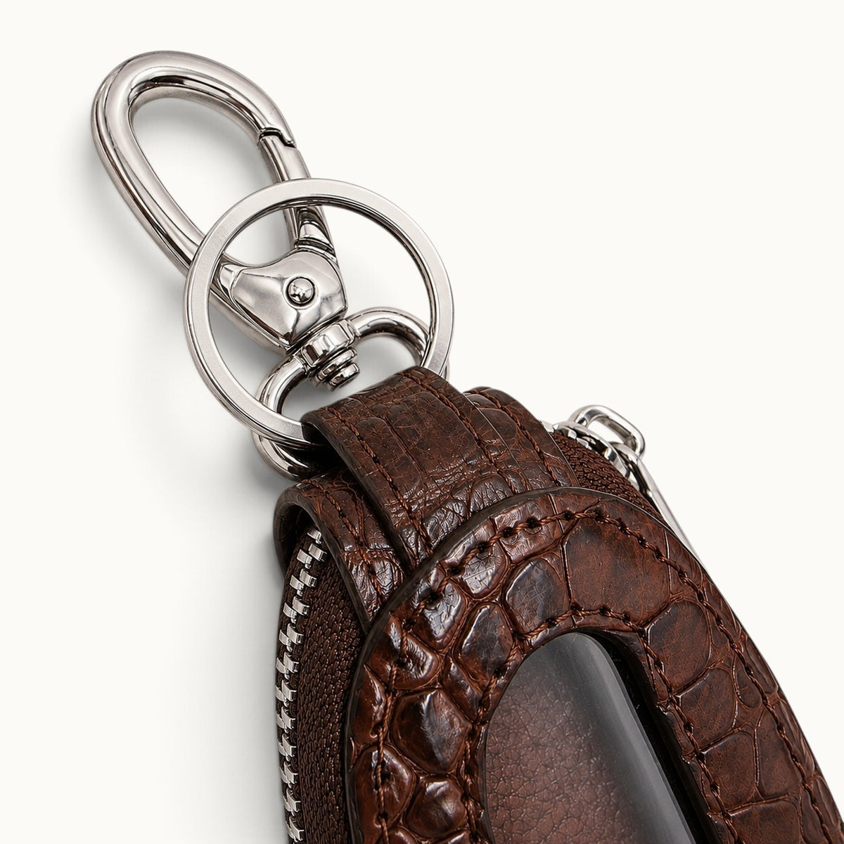 Close-up of the brown Siamensis crocodile leather car key case showing the polished brass clasp, key ring, zipper, stitching, and clear front window.