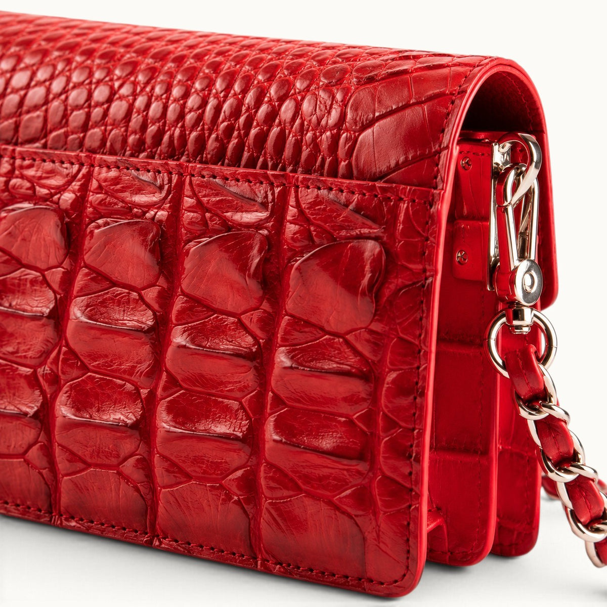 Close-up of The Chelsea red Siamese crocodile leather shoulder bag showing detailed scales, stitching, and silver-tone strap hardware.