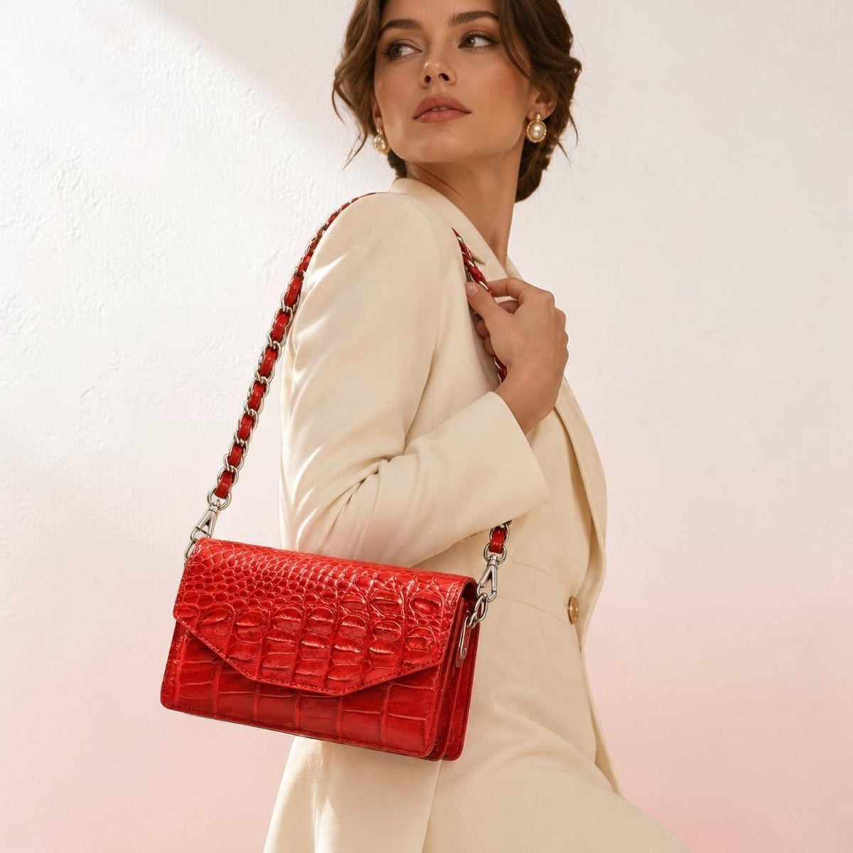 Woman in an elegant ivory suit carrying The Chelsea red Siamese crocodile leather shoulder bag with a silver-tone chain strap.