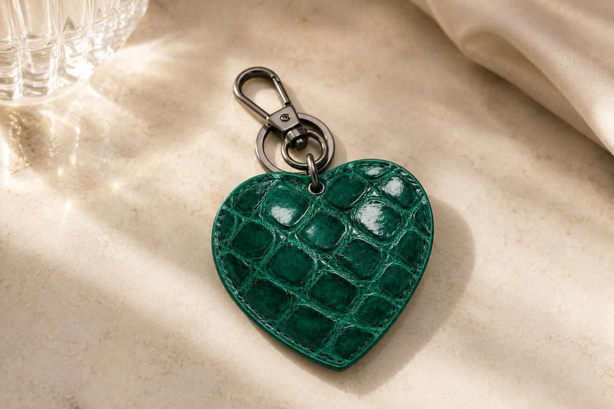 Close-up of The Heart Key Charm in emerald green Siamese crocodile leather, highlighting the natural scale pattern, stitched edges, and polished silver-tone hardware.