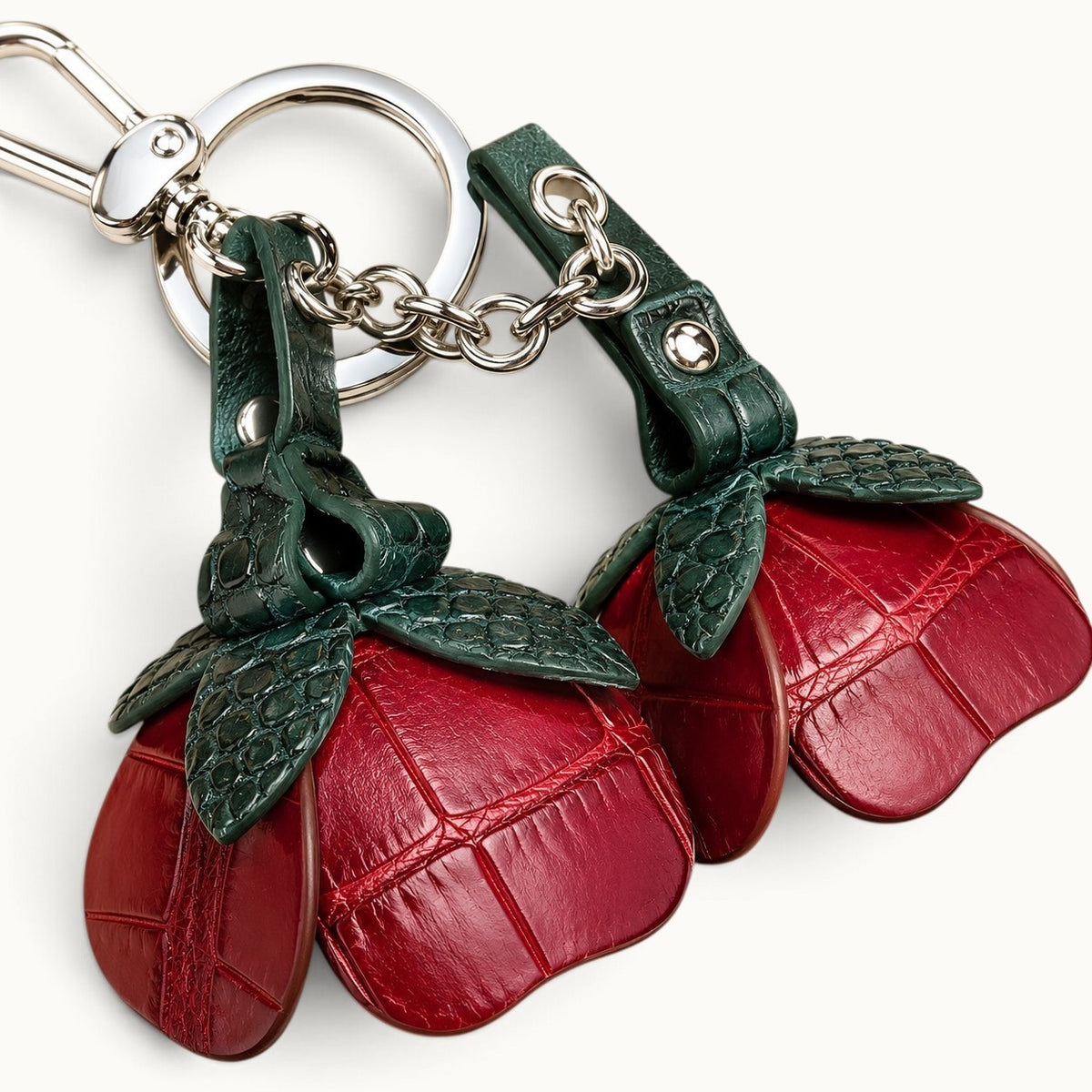 Close-up of Bordeaux Red crocodile leather scales, dark green leaves, chain, rivets, and silver-tone hardware on The Valencia charm