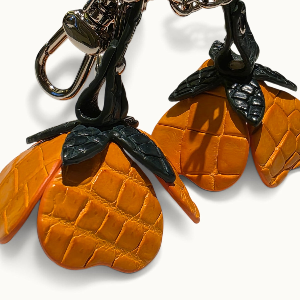 Close-up of Burnt Orange crocodile leather scales, dark green leaves, rivets, and silver-tone hardware on The Valencia charm