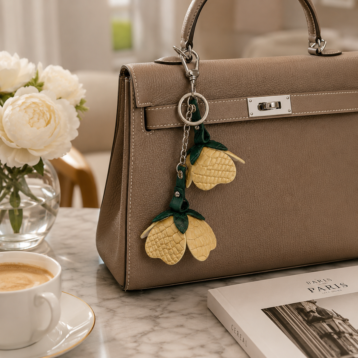 Desert Gold Valencia crocodile flower charm hanging from a taupe handbag beside coffee and flowers in an elegant lifestyle setting