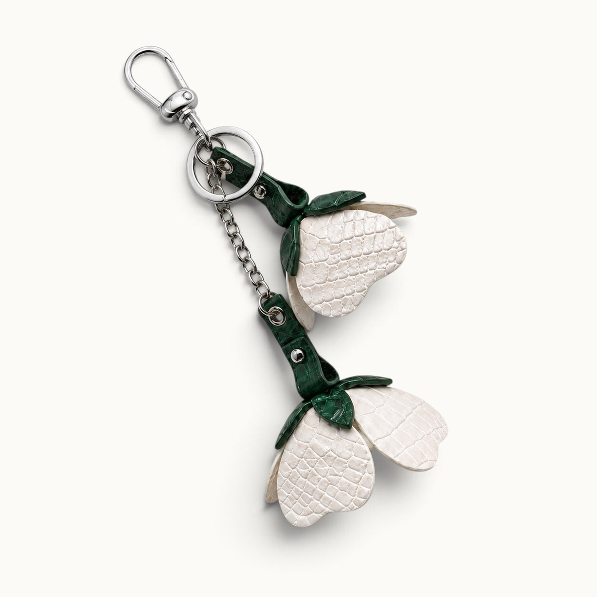 Flat-lay view of the Pearl White Valencia crocodile flower charm with dark green crocodile leather leaves, chain, ring, and silver-tone clasp